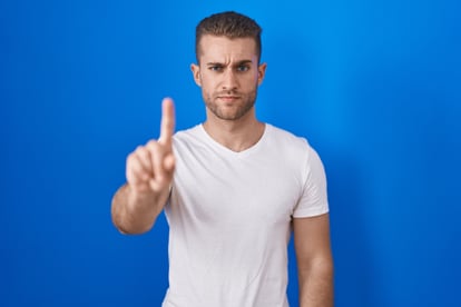 young-caucasian-man-standing-blue-background-pointing-with-finger-up-angry-expression-showing-no-gesture