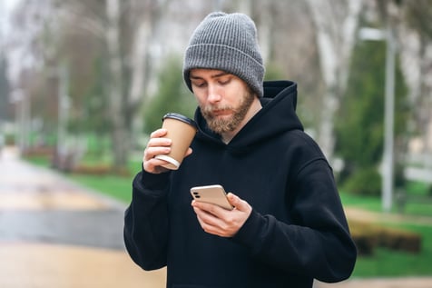 young-man-uses-smartphone-drinks-coffee-from-paper-cup-park