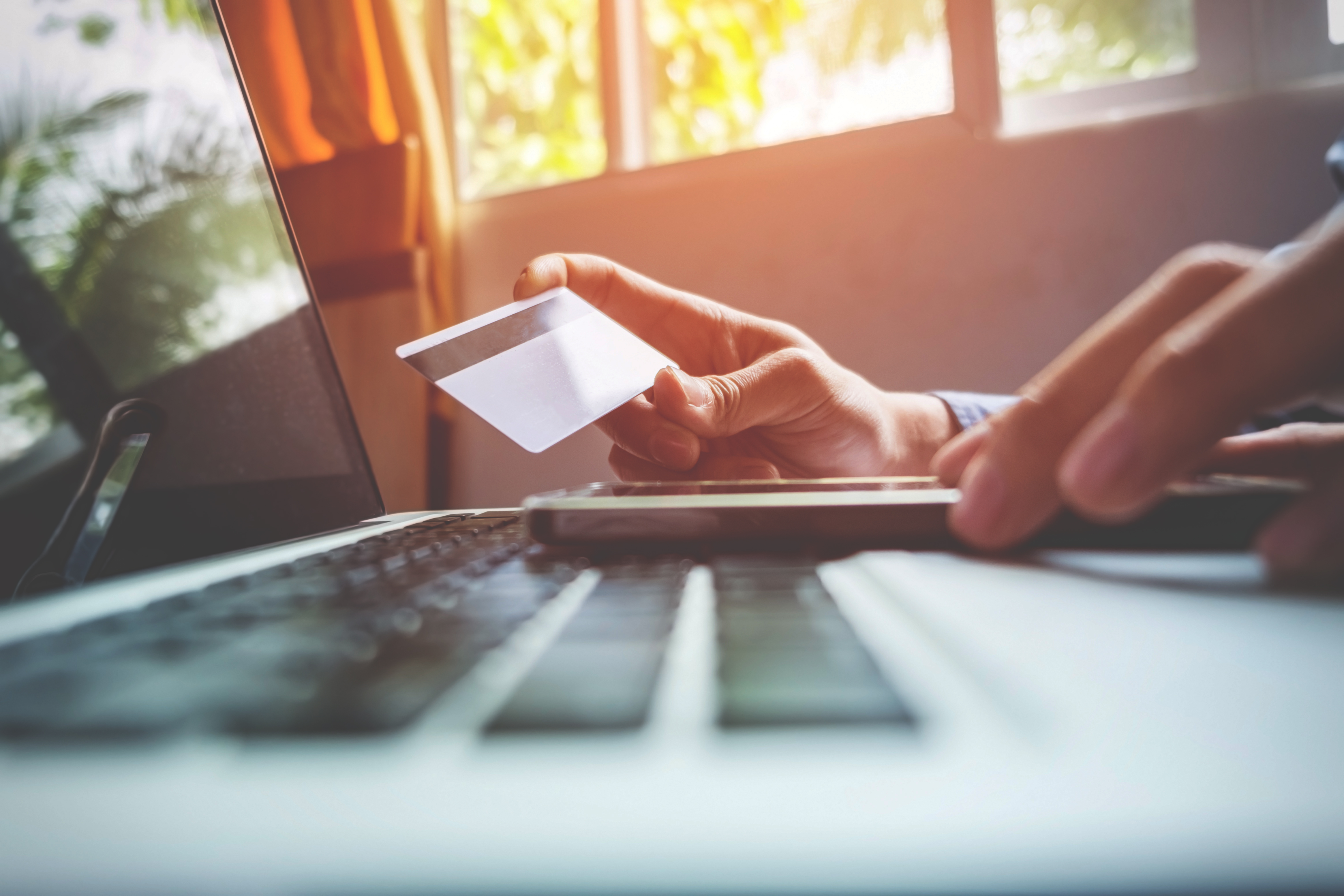 man-holding-credit-card-hand-entering-security-code-using-smart-phone-laptop-keyboard-online-shopping-concept (1)